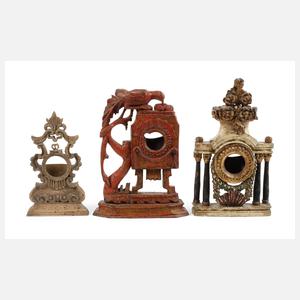 Drei geschnitzte Uhrenständer